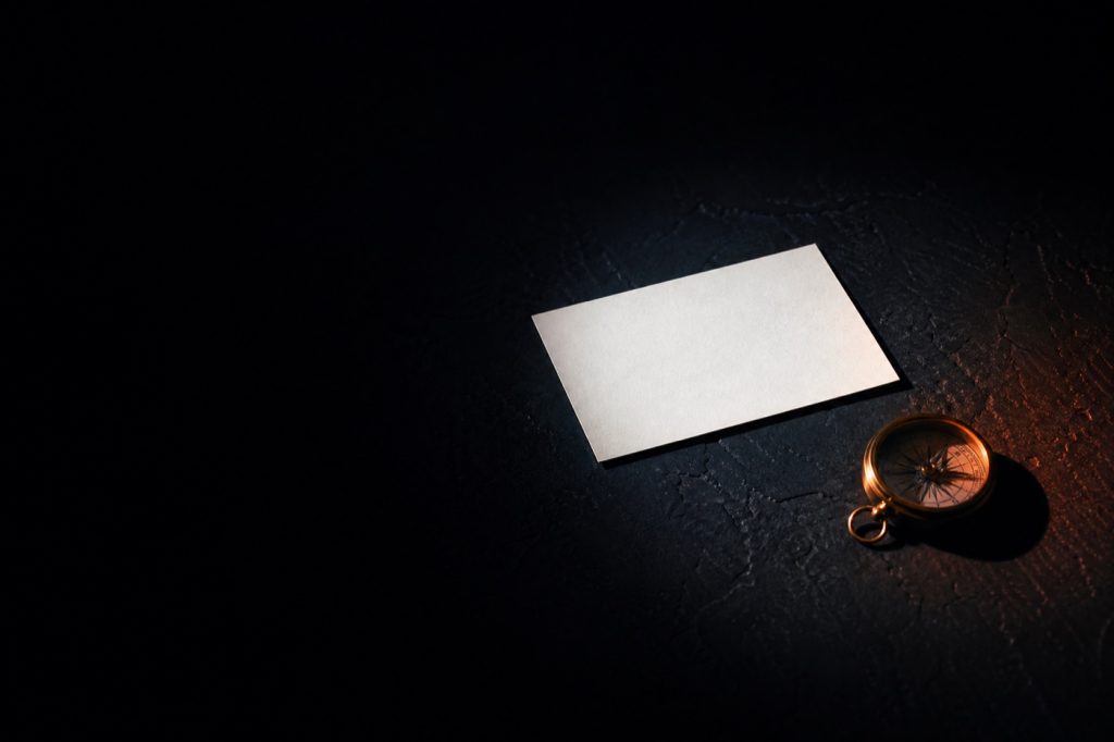 White business card and gold compass on dark stone in spotlight
